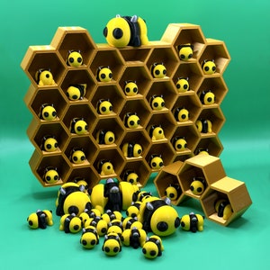 May include: A honeycomb-shaped shelf with 24 compartments, each holding a small yellow and black bee figurine. A larger bee figurine is perched on top of the shelf. Several bee figurines are scattered on a green surface below the shelf.