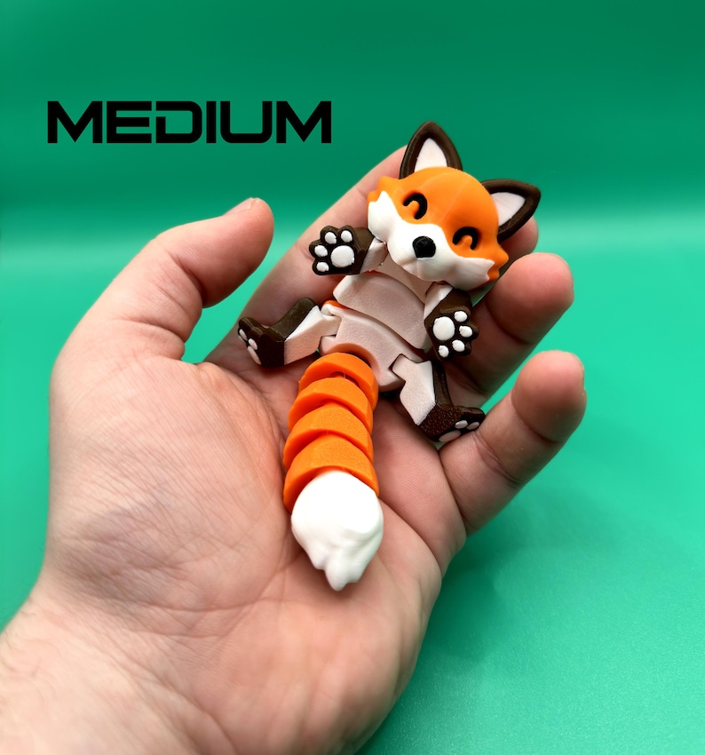 May include: A small, orange and white fox-shaped toy with a segmented tail. The toy is made of plastic and has a friendly expression. The toy is being held in a person's hand.