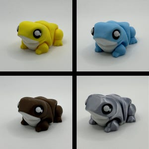 May include: Four frog figurines in yellow, blue, brown, and grey. Each frog has large, round eyes and a white underbelly. The frogs are in a playful, cartoonish style.