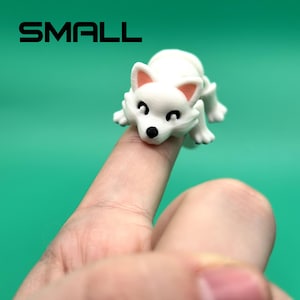 May include: White, small, plastic figurine of a dog with black eyes and pink ears. The dog is sitting on a finger.