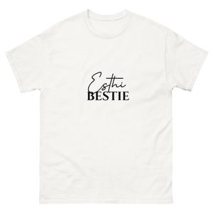 May include: A white t-shirt with the words "Esthi BESTIE" printed in black. The text is in a handwritten script font with the word "BESTIE" in a bold, sans-serif font. The shirt has short sleeves and a crew neck.