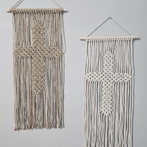 May include: Two macrame wall hangings with a cross design. The left one is beige and the right one is white.