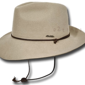 May include: A beige felt fedora hat with a brown leather band and a brown leather chin strap. The hat has a small metal tag that says "Outback" on it.