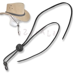 May include: A tan cowboy hat with a black leather chin strap. The strap has a black leather button and a loop at the end.