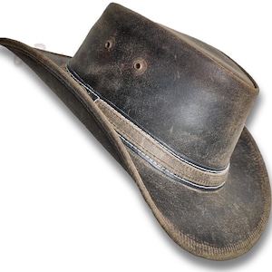 Puede incluir: Sombrero de vaquero de cuero marr&oacute;n desgastado con ala ancha. El sombrero presenta una banda decorativa con costuras blancas y dos peque&ntilde;os orificios de ventilaci&oacute;n en la corona. Dise&ntilde;ado para la protecci&oacute;n solar y actividades al aire libre.