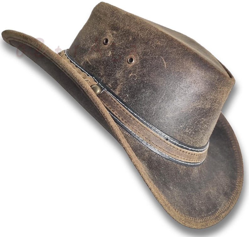 Puede incluir: Sombrero de vaquero de cuero marr&oacute;n desgastado con ala ancha. El sombrero presenta una banda decorativa con costuras blancas y detalles met&aacute;licos. Tiene dos orificios de ventilaci&oacute;n en la corona.