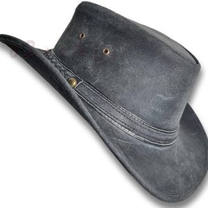Puede incluir: Un sombrero de cuero gris carb&oacute;n con ala ancha y copa ligeramente curvada. El sombrero presenta una banda decorativa con costuras blancas y un bot&oacute;n met&aacute;lico. Dos peque&ntilde;os ojales son visibles en la corona. Este sombrero es adecuado para actividades al aire libre.