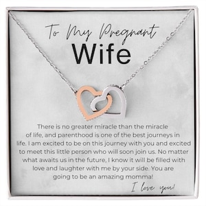 May include: A silver necklace with two interlocking heart pendants, one rose gold and one silver. The necklace is presented on a white card with the text "To My Pregnant Wife" and a loving message about parenthood.