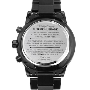 Könnte beinhalten: Eine schwarze Uhr mit einem schwarzen Armband und einem silbernen Zifferblatt. Das Zifferblatt trägt eine Botschaft, die lautet: "To My Amazing Future Husband I love you for all that you are, all that you have been, and all that you are yet to be. The true wealth of our life together lies in the time we share and the moments we create that shape our journey. As you go through the ups and downs in life, carry my love with you, knowing I will forever be by your side. Love, Your Future Wife"