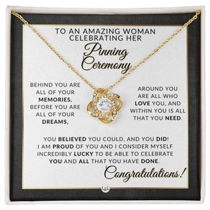 May include: A gold necklace with a crystal knot pendant presented in a gift box. The box features a message inside that reads "To an amazing woman celebrating her pinning ceremony. Behind you are all of your memories, before you are all of your dreams. Around you are all who love you, and within you is all that you need. You believed you could, and you did! I am proud of you and I consider myself incredibly lucky to be able to celebrate you and all that you have done. Congratulations!"