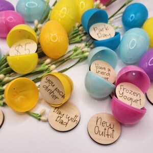 Pu&ograve; includere: Una collezione di uova di Pasqua di plastica riempite con piccoli cerchi di legno con messaggi scritti a mano. I messaggi includono "Giornata al parco", "Avere un amico", "Yogurt gelato", "Gita per il gelato", "Serata cinema a tua scelta", "Scegli tu la cena", "Giornata con pap&agrave;", e "Nuovo outfit".