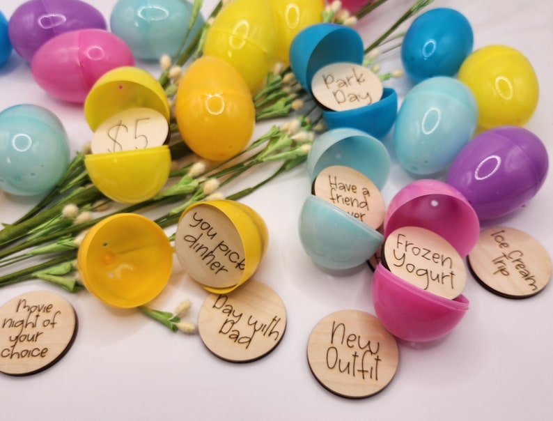 Pu&ograve; includere: Una collezione di uova di Pasqua di plastica riempite con piccoli cerchi di legno con messaggi scritti a mano. I messaggi includono "Giornata al parco", "Avere un amico", "Yogurt gelato", "Gita per il gelato", "Serata cinema a tua scelta", "Scegli tu la cena", "Giornata con pap&agrave;", e "Nuovo outfit".