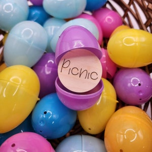 Pu&ograve; includere: Un uovo di Pasqua di plastica viola con un cerchio di legno all'interno che dice "Picnic". L'uovo &egrave; circondato da altri uova di Pasqua di plastica di vari colori, tra cui giallo, blu, rosa e azzurro.