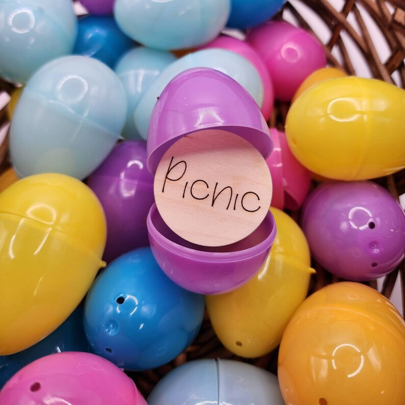 Pu&ograve; includere: Un uovo di Pasqua di plastica viola con un cerchio di legno all'interno che dice "Picnic". L'uovo &egrave; circondato da altri uova di Pasqua di plastica di vari colori, tra cui giallo, blu, rosa e azzurro.