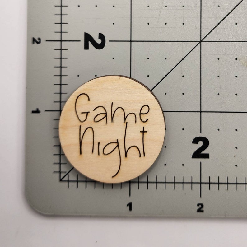 Pu&ograve; includere: Un cartello rotondo di legno con le parole "Game Night" scritte in corsivo nero.