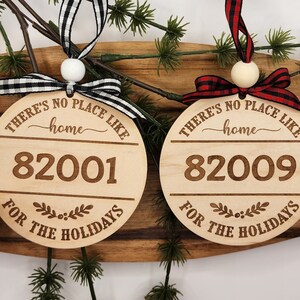 May include: Two wooden Christmas ornaments with the text "THERE'S NO PLACE LIKE home" and a year, 82001 and 82009, and the text "FOR THE HOLIDAYS". The ornaments are decorated with black and white checkered ribbon and red and black checkered ribbon.