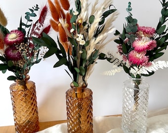 May include: Three decorative vases with dried flower arrangements. Two amber-colored glass vases have a diamond pattern, and one clear glass vase has a similar pattern. The flower arrangements include pampas grass, eucalyptus, and various dried flowers in shades of red, orange, and pink.
