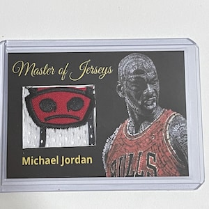 May include: A collectible card featuring Michael Jordan. The card has a jersey patch with a red and black design. The text "Master of Jerseys" and "Michael Jordan" are also visible on the card.