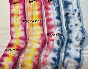 May include: Four pairs of tie-dye socks with a Nike logo. The socks are in pink and yellow, orange and yellow, red and white, and blue. The text on the socks reads "Pink/Yellow", "Orange/Yellow/Red", "Red/wht/Blue", and "Blue Tie-Dye".