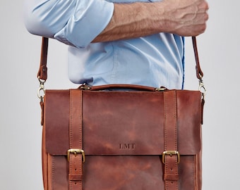 May include: A brown leather messenger bag with a long adjustable strap. The bag has two buckles on the front and the initials "LMT" are embossed on the front flap.