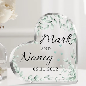May include: A clear heart-shaped acrylic keepsake with a leafy green design and the text "Mark and Nancy 05.11.2012".