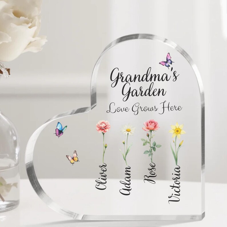 May include: A clear heart-shaped acrylic plaque with the text "Grandma's Garden Love Grows Here" and four flowers with butterflies and names "Oliver", "Adam", "Rose", and "Victoria" underneath.