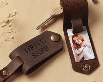 May include: Brown leather keychain with a photo insert and the words "Drive Safe" engraved on the front. The photo insert shows a woman holding a baby.