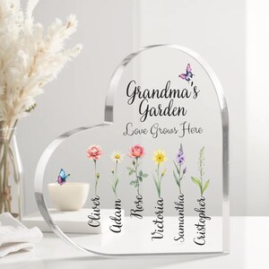 May include: A clear heart-shaped acrylic plaque with the text "Grandma's Garden Love Grows Here" and a row of colorful flowers with names below each flower: Oliver, Adam, Rose, Victoria, Samantha, Christopher.  Two butterflies are also included in the design.