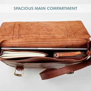 May include: A brown leather satchel bag with a spacious main compartment. The bag is open and shows a laptop, notebook, and a small zippered pouch inside.