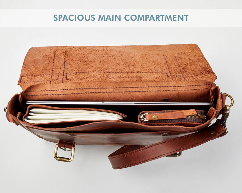 May include: A brown leather satchel bag with a spacious main compartment. The bag is open and shows a laptop, notebook, and a small zippered pouch inside.