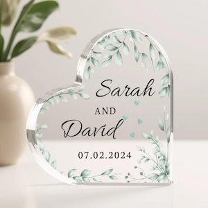 May include: A clear heart-shaped acrylic keepsake with a leafy design and the text "Sarah and David 07.02.2024".