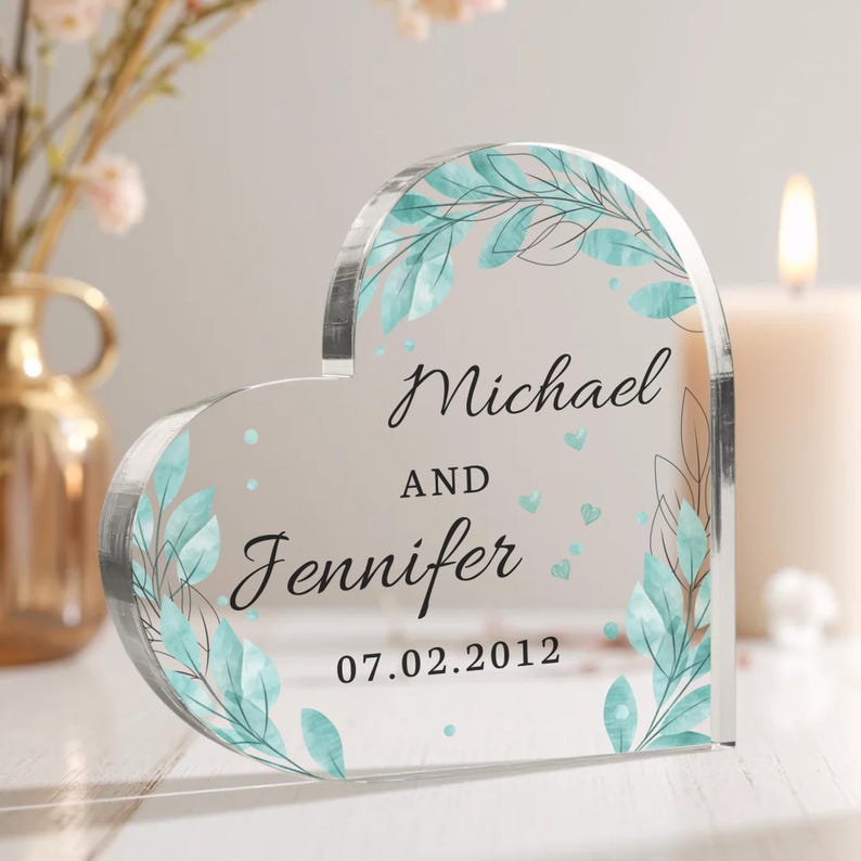 May include: A clear heart-shaped acrylic keepsake with a watercolor design of leaves and dots. The text reads "Michael and Jennifer 07.02.2012".