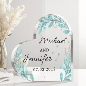 May include: A clear heart-shaped acrylic plaque with a watercolor design of teal leaves and white dots. The plaque is personalized with the names "Michael and Jennifer" and the date "07.02.2012".