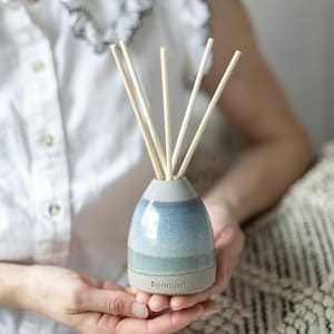 May include: A ceramic diffuser with a blue and grey glaze and wooden sticks. The diffuser is labelled "Soomish".
