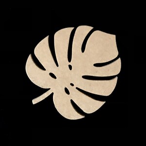 Puede incluir: Un recorte de madera de color beige claro con forma de hoja de monstera. El objeto presenta un dise&ntilde;o distintivo y sim&eacute;trico con varios recortes alargados y curvos que irradian desde el centro, imitando la nervadura natural de la planta.