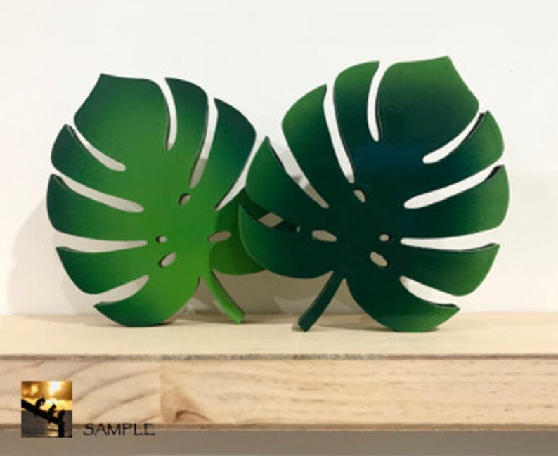 Puede incluir: Dos recortes decorativos en forma de hoja de monstera que presentan un degradado de tonos verdes, desde el m&aacute;s claro al m&aacute;s oscuro. Cada hoja muestra el dise&ntilde;o caracter&iacute;stico de la planta monstera con sus divisiones y perforaciones.