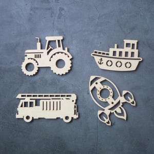 May include: Four wooden cutouts of transportation vehicles: a tractor, a ship with an anchor, a fire truck, and a rocket ship. The cutouts are light brown and set against a dark gray background.
