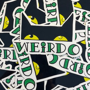 May include: A black cat with green eyes and the word "WEIRDO" written in green and white letters on a white background. The cat is wearing a white collar with a green stripe.