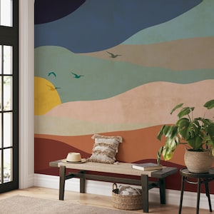 May include: A wall mural with a sunset landscape design featuring a yellow sun, blue, green, and brown hills, and flying birds. A wooden bench with a cushion and a woven basket are in the foreground.