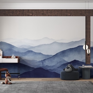 May include: A watercolor mountain range mural in shades of blue, gray, and white, with a brown wooden frame. The mural is on a white wall in a room with a desk, chair, and a plush gray beanbag chair.