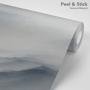 May include: A roll of peel and stick wallpaper with a textured surface. The wallpaper features a misty mountain landscape in shades of blue and gray.
