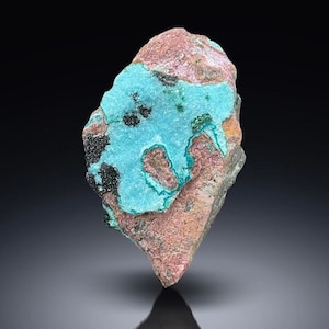 May include: A rough, irregularly shaped rock with a large patch of bright blue-green mineral. The mineral has a crystalline texture and is surrounded by a reddish-brown matrix.