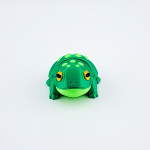May include: A green 3D printed frog figurine with yellow eyes and a textured surface.