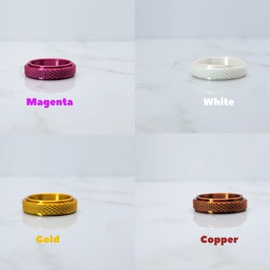 May include: Four different colored rings with a textured surface. The rings are magenta, white, gold, and copper.