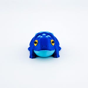 May include: A blue and light blue 3D printed frog figurine with yellow eyes.
