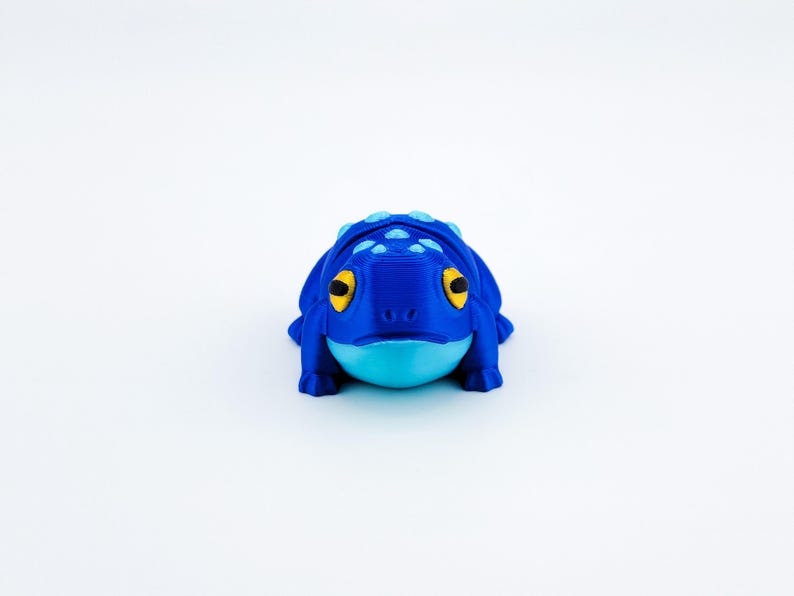 May include: A blue and light blue 3D printed frog figurine with yellow eyes.