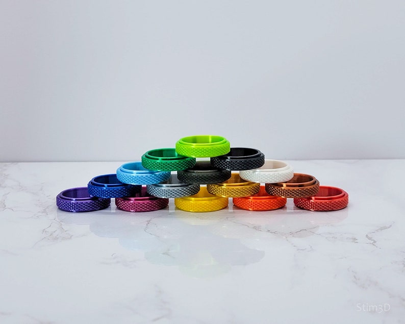 May include: A stack of 14 colorful rings, arranged in a pyramid shape, with a green ring at the top. The rings are made of a smooth, shiny material and have a textured surface.