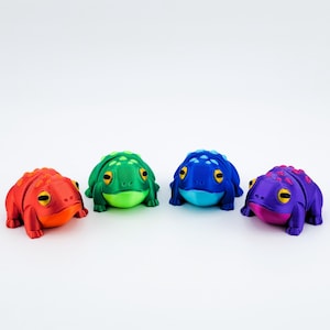 May include: Four small frog figurines in different colours: red, green, blue, and purple. Each frog has a textured surface and black eyes.