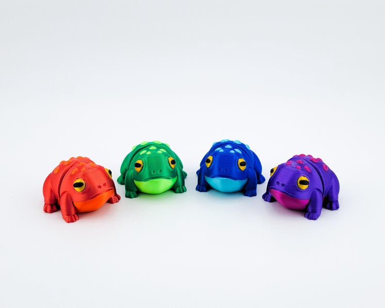 May include: Four small frog figurines in different colours: red, green, blue, and purple. Each frog has a textured surface and black eyes.