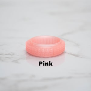 May include: A pink ring with a textured surface and the word "Pink" in black text. The ring has a series of small, raised bumps around its outer edge. The ring is made of a translucent material.